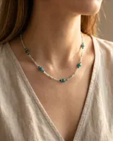 Collar de acero con baño de oro, compuesto por una delicada cadena de pequeñas cuentas en tonos celestes y verdes, intercaladas con piedras naturales redondas de mayor tamaño en color turquesa y verde oscuro.
