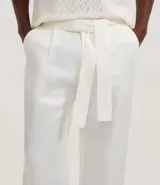 Pantalón de sastrería corte wide leg color blanco, confeccionado en una mezcla de liocel y lino. Presenta cintura con trabillas, cierre tradicional, bolsillos laterales y cinturón de tela con lazo ajustable.