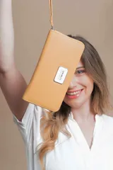 Billetera larga con cierre perimetral, confeccionada en material sintético texturizado color mostaza. Cuenta con correa de mano extraíble y placa metálica con logo de la marca en el frente.