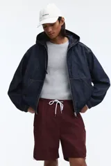 Short deportivo de nylon color bordó, con franjas laterales blancas, cintura elástica con cordón de ajuste blanco y bolsillos laterales.