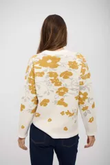 Buzo de tejido de punto con diseño estampado de flores en tonos mostaza y gris sobre fondo blanco. Presenta cuello redondo, mangas largas y corte recto.