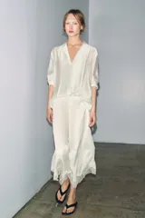 Camisa fluida de corte recto con acabado satinado, escote en pico y manga larga con puños anchos. Presenta un diseño minimalista con costuras verticales frontales.