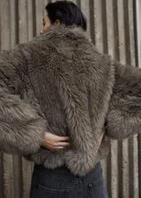 Chaqueta corta de piel sintética con textura mullida, cuello solapa grande y mangas largas.