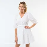 Vestido corto blanco con diseño de bordado inglés, escote en V con botones frontales, mangas abullonadas tres cuartos y detalle de lazo ajustable en la cintura con falda escalonada.