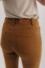 Pantalón de jean color marrón óxido, tiro medio, corte ajustado en muslos y ligeramente acampanado en la parte inferior (bootcut/flare), con bajo desflecado.