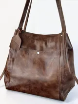Bolso tipo tote grande de cuero genuino marrón, con asas de hombro dobles, bolsillo exterior con botón a presión y llavero colgante con la marca grabada.