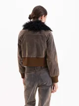 Campera estilo bomber de silueta entallada, confeccionada en tela Denim Velvet con acabado visual de jean y tacto de terciopelo. Presenta cuello desmontable de pelo sintético, cierre frontal con botones, bolsillos superiores y puños y cintura de tejido elástico acanalado.
