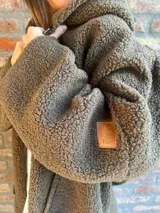 Campera de corderito color verde oscuro, con diseño holgado, cuello alto y manga larga. Presenta una etiqueta de cuero sintético en la manga.