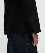 Blazer de sastrería confeccionado en tejido de poliéster con acabado liso. Presenta un diseño de corte regular con solapas clásicas, cierre frontal de un botón y mangas largas con botones forrados en los puños. Incluye bolsillos con solapa y forro interior.