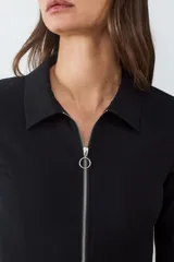 Campera de manga larga confeccionada en tejido crepé, con cuello camisero y cierre frontal metálico completo. Presenta un diseño entallado y moderno con mangas ligeramente acampanadas.