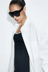 Camisa oversize de cuello solapa, manga larga con hombro caído y puños con pliegues. Presenta un bolsillo de plastrón en el frente, detalle de pinza con trabilla y botón en la espalda, bajo asimétrico y cierre frontal con botones.