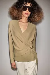 Chaqueta de punto de color tostado, con escote en V y manga larga. Diseño cruzado al frente con cinturón lazada en el mismo tejido y detalle de hebilla metálica circular en el lateral.