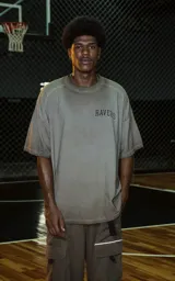 Remera de manga corta y cuello redondo, calce oversize, color marrón oscuro con efecto batik/lavado. Presenta un pequeño bordado o aplique con la palabra "RAVERS" en el pecho.