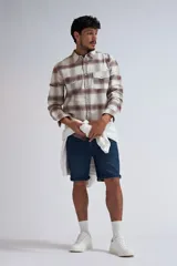 Camisa de manga larga a cuadros color beige y marrón, con cuello clásico, cierre frontal con botones a presión, dos bolsillos con solapa abotonada en el pecho y puños abotonados.