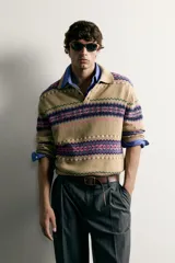 Sweater de punto jacquard de algodón y lino, color tostado con diseño de franjas geométricas en tonos violeta, fucsia y verde. Presenta cuello polo con cierre frontal de tres botones, mangas largas y puños y cintura en rib.