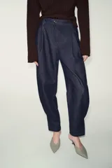 Pantalón de denim azul oscuro, tiro alto, con pinzas delanteras que generan volumen en la cadera y pernera ancha y recta. Presenta cierre frontal y bolsillos laterales.