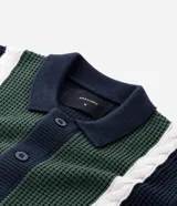 Cardigan masculino de punto con cuello camisero y cierre frontal de botones. Presenta un diseño con paneles frontales en color verde y blanco que contrastan con el cuerpo azul marino, destacando por su textura de tejido diferenciada.
