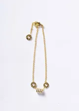 Pulsera de cadena fina en plata 925 con baño de oro 18k. Presenta un dije central cilíndrico con zirconias incrustadas, flanqueado por dos arandelas circulares con números romanos grabados.