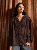 Blusa de tela liviana color marrón, con escote en V, mangas largas con puños y detalles de bordado floral tono sobre tono en toda la prenda.