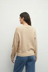 Sweater de tejido de punto color marrón, con cuello redondo y detalles de calados decorativos en el cuello y las mangas. Presenta un diseño de corte recto y manga larga.
