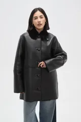 Tapado de eco-cuero negro con interior y cuello de piel sintética, cierre frontal con botones y diseño holgado.