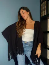 Ruana tejida a mano en punto arroz con lana merino, presenta un diseño envolvente con flecos en los extremos.