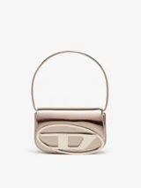 Bolso pequeño de cuero bovino con acabado espejado brillante color oro rosado. Presenta un asa corta para llevar al hombro y una solapa frontal con la placa ovalada con el logo 'D' de Diesel en metal galvanizado.