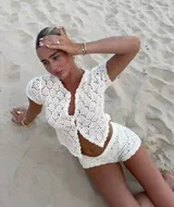Conjunto de dos piezas tejido en crochet color blanco, compuesto por una camisa de manga corta con cierre frontal de botones y un short de tiro alto.