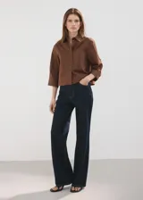 Camisa de algodón color marrón, de diseño recto, con cuello camisero, manga larga con puños abotonados y cierre delantero con botones.