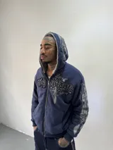 Campera reversible con cierre frontal. Un lado confeccionado en algodón azul marino con estampa plastisol, bordados con apliques y capucha. El otro lado presenta un diseño de polar de pelo largo en color gris. Posee corte oversize, puños y ruedo acanalados.