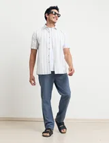 Camisa de manga corta a rayas verticales color natural y celeste, con cuello clásico, cierre frontal con botones de madera y bolsillo de parche en el pecho.