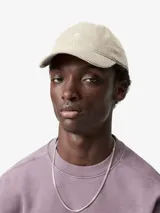 Gorra de seis paneles confeccionada en corderoy de canal ancho, con visera curva, tira regulable con hebilla metálica y logo bordado en el frente.