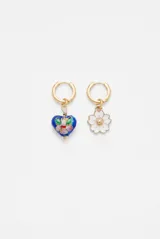 Aros abridores dorados con dijes colgantes asimétricos: un corazón azul con diseño floral esmaltado y una flor blanca con centro dorado.