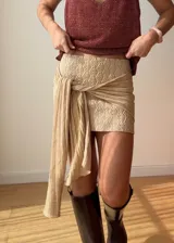 Mini falda de punto color marrón con textura tejida, diseño ajustado y detalle de lazo lateral largo que cae sobre la pierna.