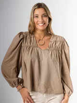 Blusa color beige con escote cuadrado y textura drapeada al frente. Sus mangas largas abullonadas aportan volumen y frescura.