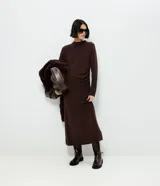 Vestido midi de punto color marrón chocolate, con manga larga, cuello alto sutil y detalle de fruncido lateral que ajusta la silueta. Diseño minimalista de corte recto.