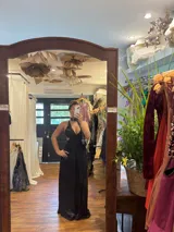 Vestido largo con estampado tie-dye en tonos violeta y fucsia, escote en V con detalles bordados dorados, cut-outs laterales bajo el busto y tirantes finos que se cruzan y atan en la espalda.