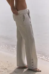 Pantalón de tiro medio con estampado de rayas verticales, confeccionado en mezcla de lino. Presenta trabillas, cinturón del mismo tejido para anudar en la cintura, cierre frontal con cremallera y botón, y detalle de abertura con botones en el bajo.