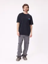 Remera de algodón con calce oversize, color negro con efecto lavado. Presenta un estampado gráfico en la espalda con diseño de espiral en tonos rosado y celeste, acompañado de inscripciones decorativas.