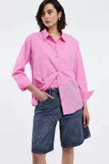 Camisa oversize de popelina a rayas celestes y blancas, con cuello camisero, manga larga con puños abotonados, cierre frontal con botones y un bolsillo en el pecho con etiqueta bordada.