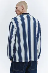 Camiseta de fútbol de manga larga confeccionada en malla estampada, con diseño de rayas verticales en azul marino y blanco. Presenta cuello polo negro con ribete blanco, cierre frontal parcial en V, y puños elásticos negros con líneas blancas. Cuenta con estampado frontal con gráficos de estrellas y la inscripción "Run Wild".
