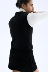 Chaleco negro de pana, con escote en V y cierre frontal de tres botones. Es una prenda entallada y forrada.