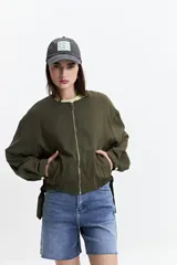Campera verde militar sin cuello, con elástico y cinto regulable en la cintura, bolsillos amplios y cierre frontal.