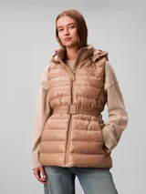 Chaleco puffer acolchado color tostado de la marca Calvin Klein, con diseño sin mangas, cuello alto y capucha desmontable. Cuenta con cierre frontal de cremallera y un cinturón elástico ajustable con hebilla de clip con el logo de la marca.