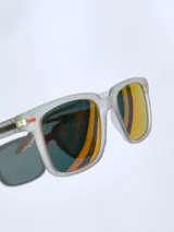 Lentes de sol con armazón de acetato traslúcido en acabado mate y cristales polarizados con efecto espejado en tono naranja. Presentan detalles en color naranja en las patillas y el frente.