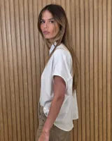 Camisa de manga corta color beige, de corte holgado, con cuello camisero y cierre frontal de botones.