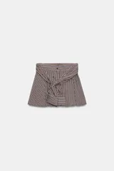 Bermuda de tiro medio con estampado de rayas verticales en tonos marrones y celestes. Presenta un diseño único con lazada frontal que simula mangas anudadas, elástico en la parte posterior de la cintura, cierre frontal con cremallera y botones, y bajo con vuelo.