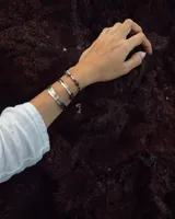 Pulsera tipo esclava abierta con diseño rústico y acabado irregular, fabricada en bronce y alpaca.