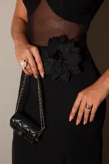 Vestido largo de fiesta negro, con breteles finos, corpiño con copas y transparencias en la zona del abdomen. Presenta un aplique de flor en la cintura y tajo lateral en la falda.