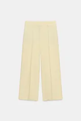 Pantalón cropped de tiro medio color amarillo pastel, perteneciente a la colección Zara Woman Collection. Presenta diseño de pierna ancha, trabillas en la cintura, bolsillos laterales ocultos y pinzas en el delantero. Cuenta con cierre frontal con cremallera, botón y ganchos metálicos.